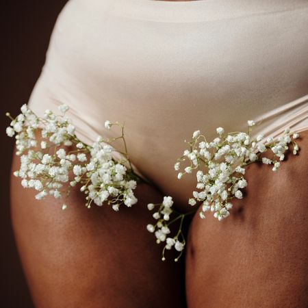 Weiblicher Unterleib mit weißen Blumen, die seitlich aus der Unterhose herausschauen